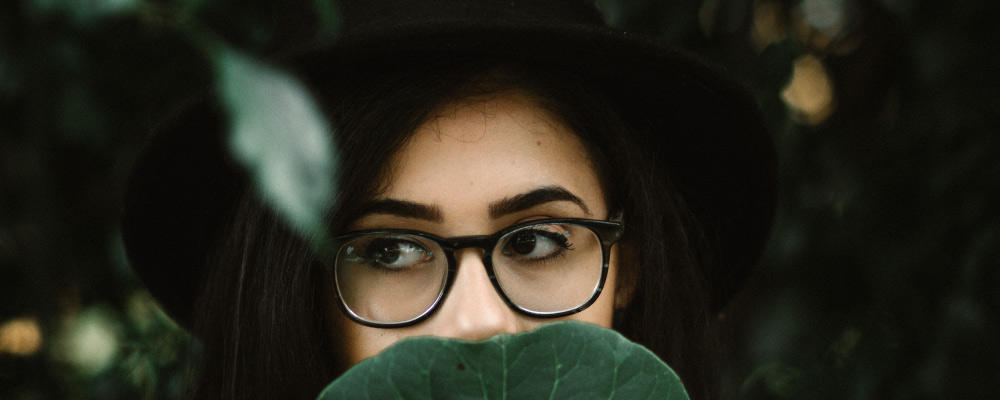 Girl With Glasses Covering Mouth With Leaf